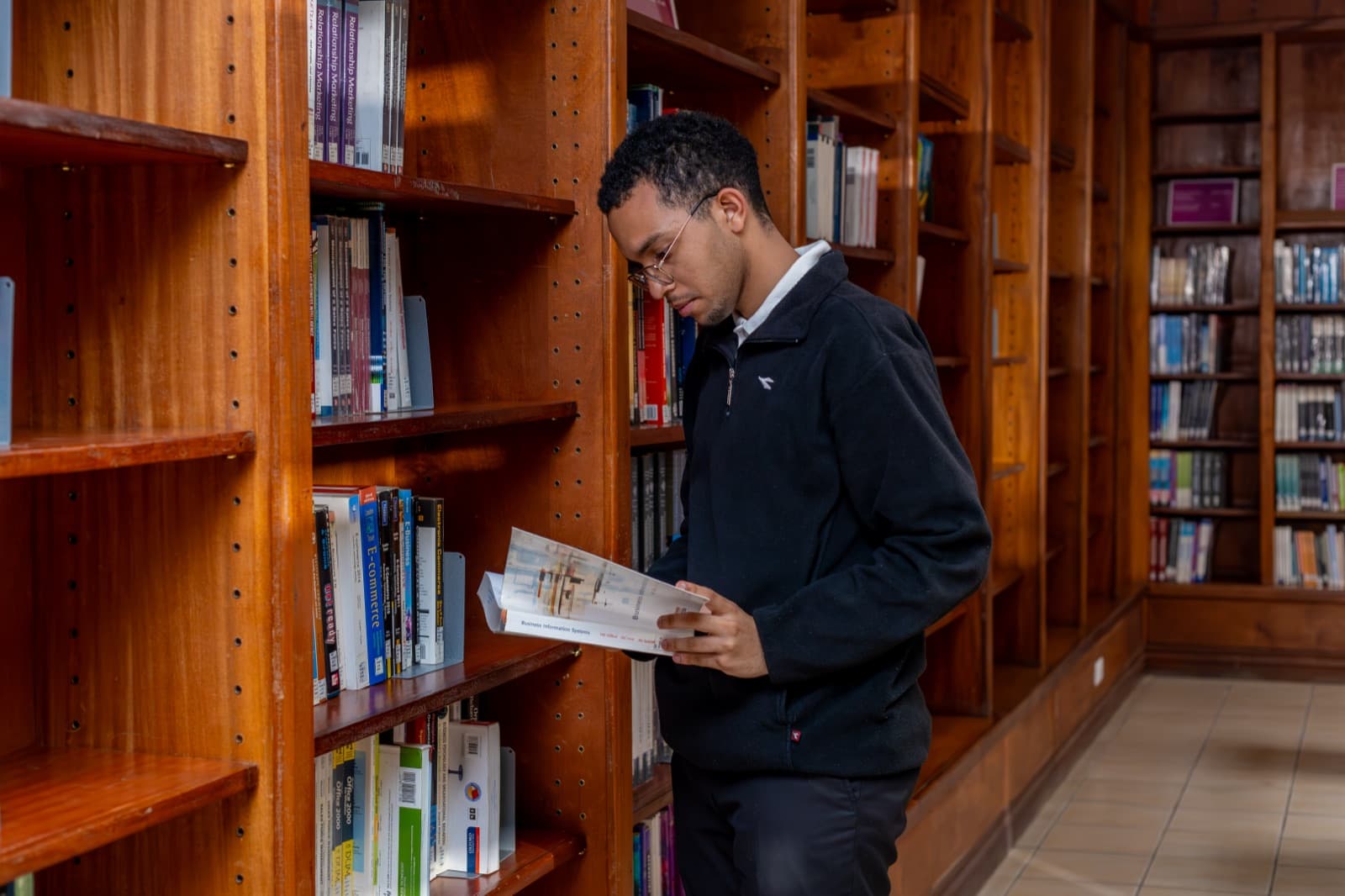 A student reading a book among the shelves in Riara University Library
