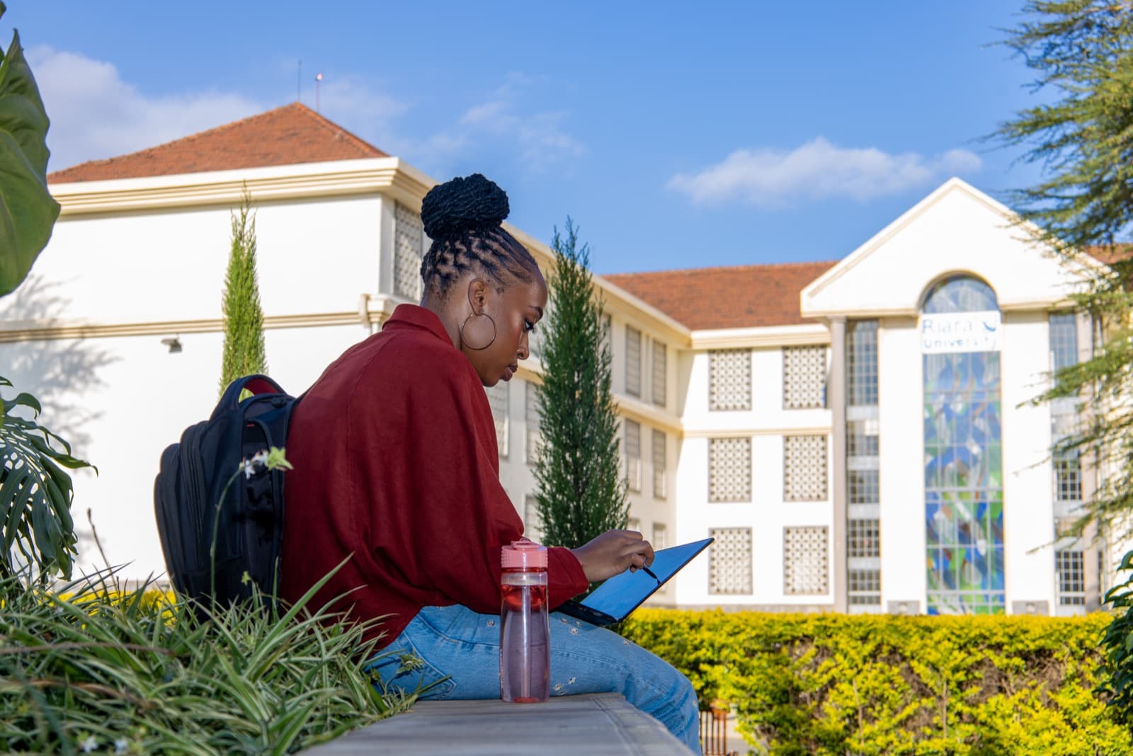 A student reading on a tablet outside on the Riara University campus